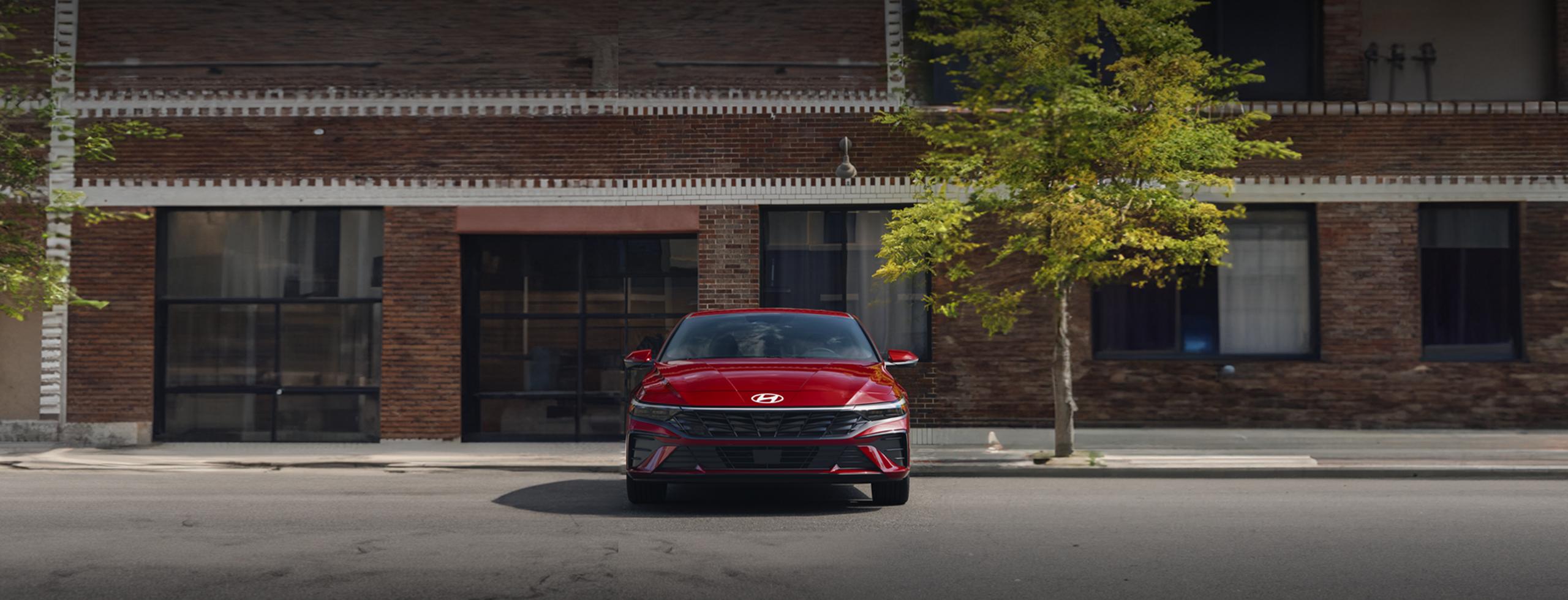 Vista frontal del nuevo Elantra 2025, en color rojo, estacionado en la calle