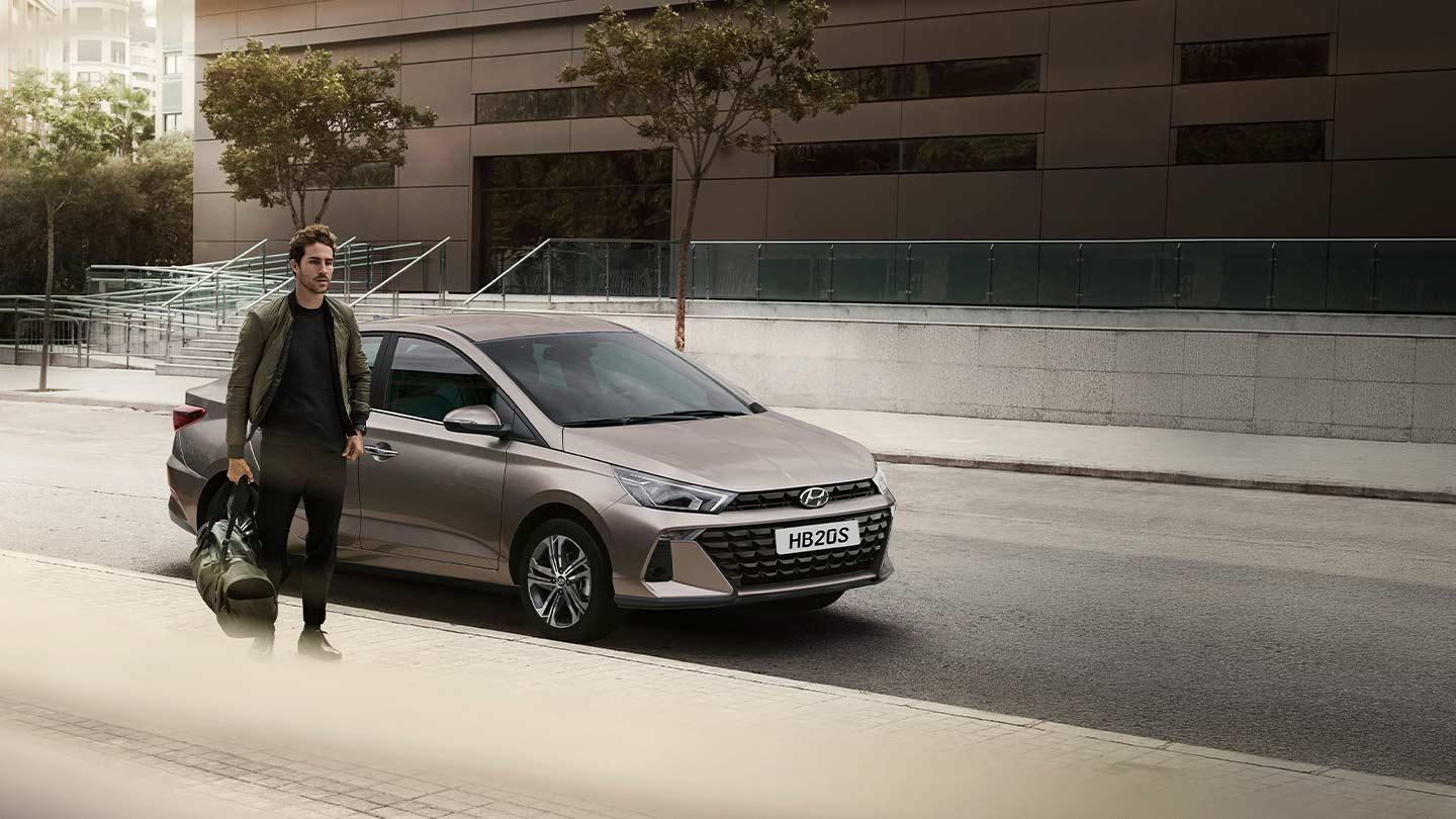 Hombre caminando con una maleta junto a Hyundai HB20 Sedán color gris