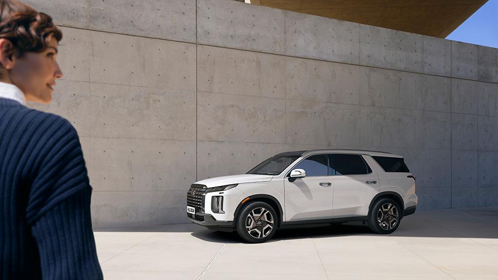 Mujer de espaldas en primer plano con Hyundai Palisade color blanca frente a ella